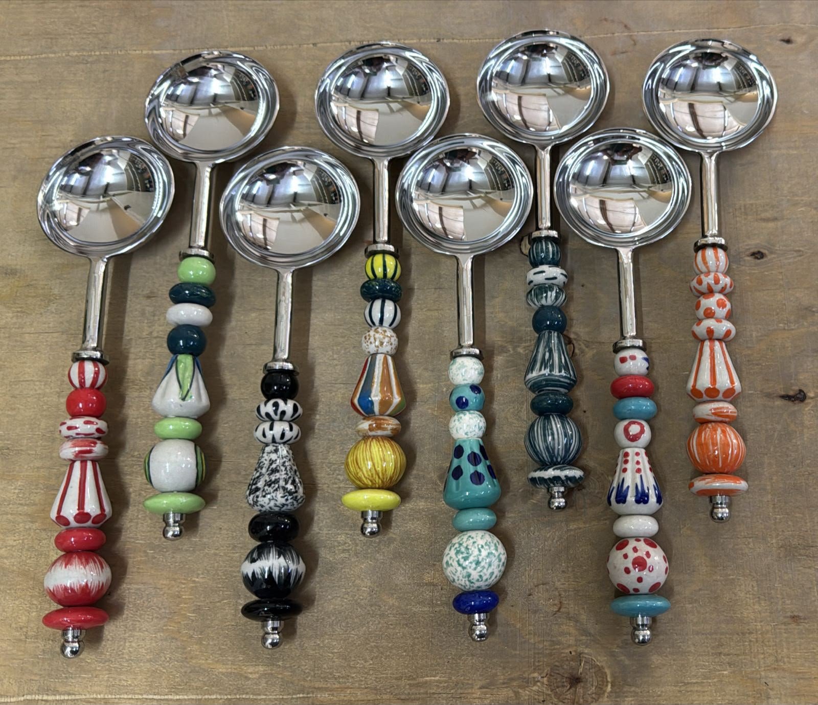 Nine serving spoons with hand-painted ceramic beaded handles in different colours.